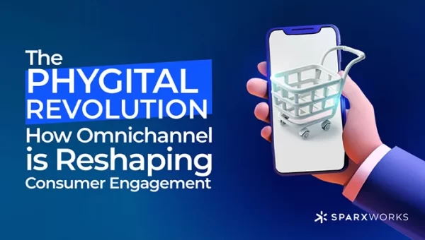 A digital graphic on a dark blue background with the text "The Phygital Revolution: How Omnichannel is Reshaping Consumer Engagement" in white letters. On the right, a stylized hand in a suit jacket holds a smartphone with a 3D rendered shopping cart icon on the screen. The Sparxworks logo is in the bottom right corner.