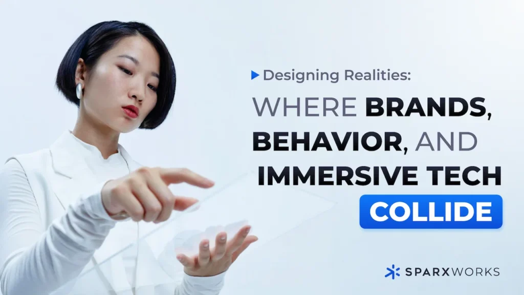 A person with short dark hair and a light complexion, wearing a white collared shirt, appears to be interacting with a translucent digital interface floating between their outstretched hands. The background is a bright, gradient white to light blue. To the right of the person, large, bold text reads "Designing Realities: WHERE BRANDS, BEHAVIOR, AND IMMERSIVE TECH COLLIDE". Below this text is a blue rectangular box containing the word "COLLIDE" in white, bold lettering. At the very bottom right, the Sparxworks logo is visible.